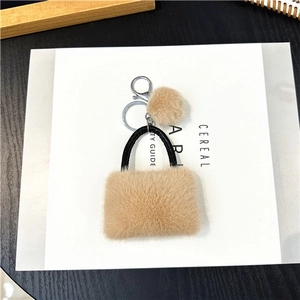 Detail of plush handbag keychain in khaki faux fur with leather handle on magazine