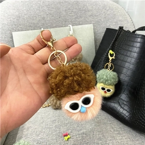 Close-up of a plush doll keychain with brown curly hair and white frame sunglasses
