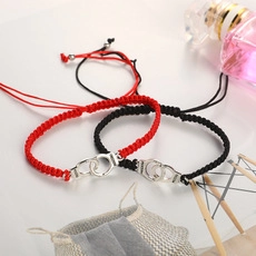 Detalle de pulseras tejidas rojas y negras con esposas de acero inoxidable