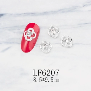 Macro detail of clover-shaped nail charms with pearls and rhinestones on a red nail