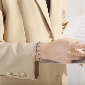 Macro detail of silver knot design bracelet on model wrist with beige blazer
