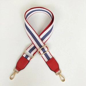 Close-up of adjustable striped handbag strap with red leather ends and gold buckles