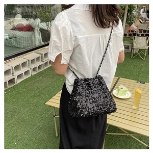 Detail of a sparkling black sequin bucket bag with a silver chain strap on a lady