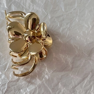 Detailed view of a golden metal flower hair claw clip on a soft white background