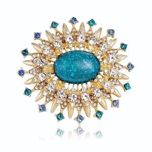 Detail of sunburst brooch with emerald green gemstone and sparkling crystals on gold metal