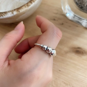 Detailed view of silver minimalist ring with multiple beads worn on finger over wood
