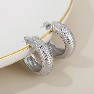 Macro detail of thick silver hoop earrings featuring a textured scale pattern on a dish