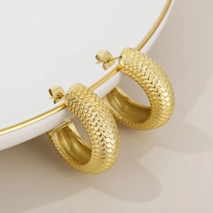 Detailed close-up of 18K gold stainless steel C-shape earrings with scale texture on a plate