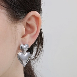 Close-up of dual silver heart-shaped stainless steel earrings worn by a model