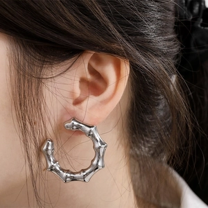 Close-up of silver hollow bamboo-shaped C hoop earrings worn on a model's ear