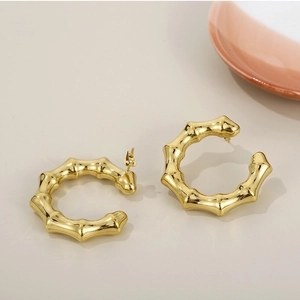 Polished 18K gold plated stainless steel C-shape bamboo hoop earrings on beige surface