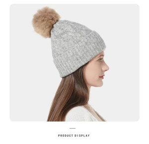 Close-up of light gray cable knit beanie with a brown faux fur pom-pom on a model