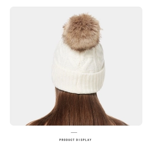 Detail of off-white knit beanie featuring a large brown faux fur pom-pom and thick cuff