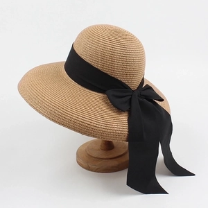 Close-up of straw sun hat showing brown weaving detail and elegant black ribbon bow