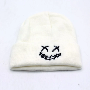 Detailed close-up of white cuffed beanie with black embroidered smiley face and X eyes