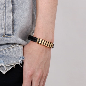 Detail of men's double-layer black leather braided bracelet with gold metal accents