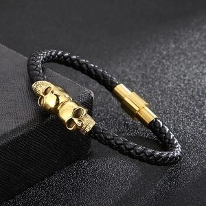 Detail of black braided leather bracelet featuring golden skull charms and magnetic clasp