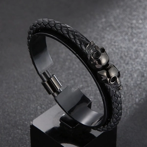 Detailed close-up of a black braided leather bracelet featuring two steel skull charms