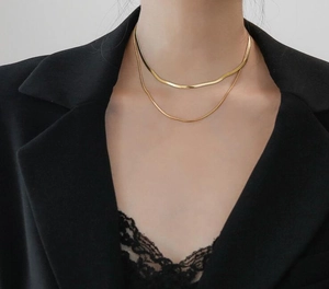 Close-up of double-layered gold snake chain and thin link necklace on model wearing black
