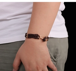 Close-up of a brown woven nylon rope bracelet with a rose gold anchor-shaped clasp