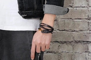 Detail of a multi-layer black leather bracelet with a gold metal hook clasp on wrist