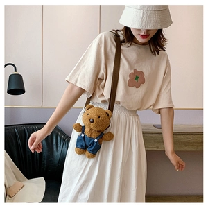 Detail of cute brown plush bear crossbody bag with denim overalls on a white skirt