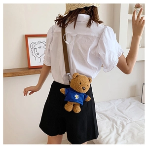 Detail shot of a plush brown teddy bear crossbody bag with a blue daisy shirt
