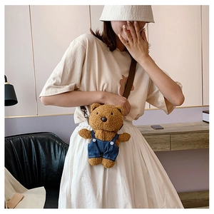 Brown teddy bear plush crossbody bag with denim overalls worn by a model in a cozy setting