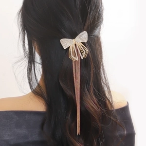 Detail of a sparkling rhinestone bow hair clip with long metal tassels on a hair style