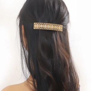 Detail of a hollow gold rectangular hair clip with diamonds on dark hair