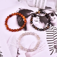 Detalle de pulseras elásticas de piedra natural con cuentas marrones, ojo de tigre y blancas