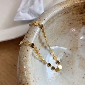 Macro shot of polished gold disc chain links hanging on a minimalist ceramic bowl edge