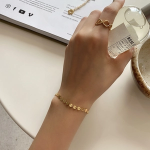 Close-up of a gold disc chain bracelet and infinity ring set worn by a model