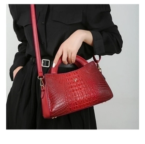 Close-up of a red crocodile pattern handbag featuring a gold V-shaped metal logo detail