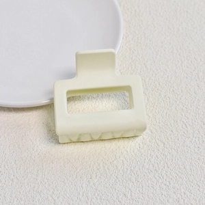 Detail view of a square matte cream hair claw clip with cutout design on textured surface