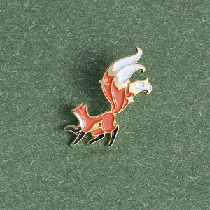 Detailed view of an orange fox enamel pin on green textured paper background