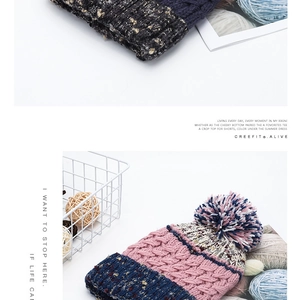 Detailed close-up of thick knit winter beanie with contrasting pom-pom and gold silk yarn