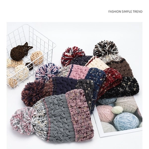 Close-up of colorful knit beanies with large pompoms in a white decorative basket
