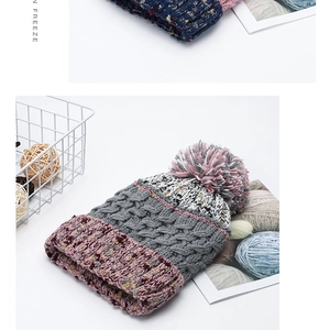 Detail of chunky knit beanie with contrast pompom and colorful tiered patchwork texture
