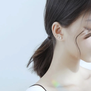 Close-up of a model wearing four graduated sizes of white round pearl stud earrings