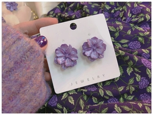 Macro view of purple gardenia flower earrings with a pearlescent finish on white card