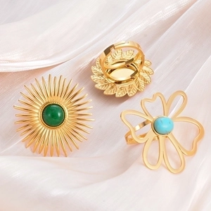 Three vintage turquoise stainless steel rings on beige silk, featuring sun and flower motifs