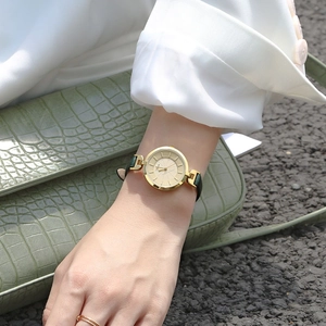 Close-up of elegant gold round dial watch with green leather strap on a model's wrist