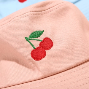 Gros plan sur un bob en coton rose avec broderie cerise détaillée et coutures du bord