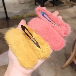 Close-up of a hand holding four soft plush hair clips in pink and yellow colors