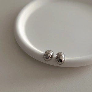 Macro view of polished silver bean-shaped stud earrings on a minimalist white ceramic tray