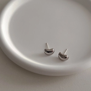 Polished silver bean stud earrings for women on a white minimalist ceramic tray