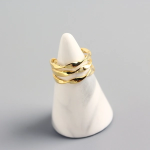 Detail of a layered golden twisted ring displayed on a white marble cone stand