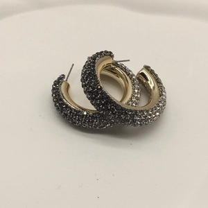 Detail shot of C-shaped gold earrings with dark rhinestones on a minimalist background