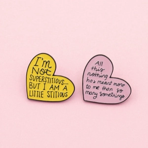 Detail of heart enamel pins with motivational quotes on a soft pink background